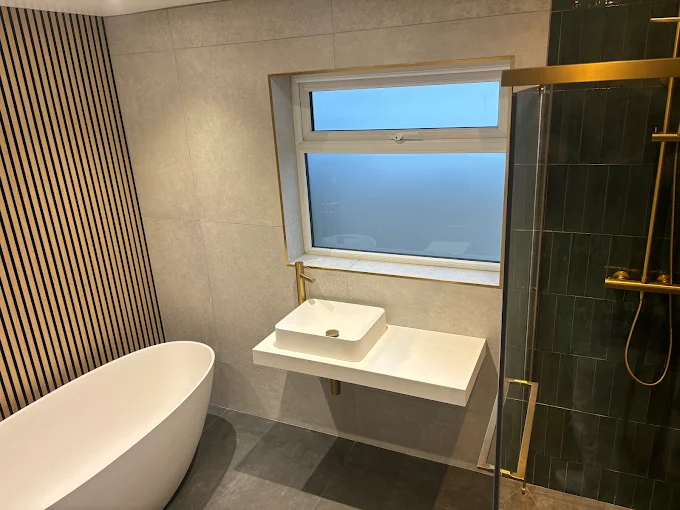 Modern bathroom with freestanding bath, brushed gold fittings and green tiled shower
